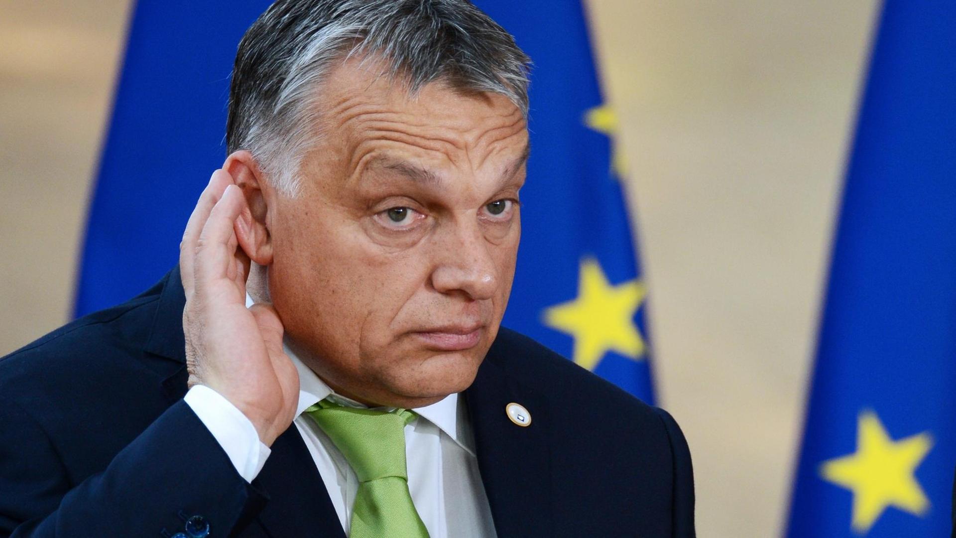 Viktor Orbán hält sich lauschend die rechte Hand hinter das Ohr, im Hintergrund eine EU-Fahne Viktor Orbán hält sich lauschend die rechte Hand hinter das Ohr, im Hintergrund eine EU-Fahne