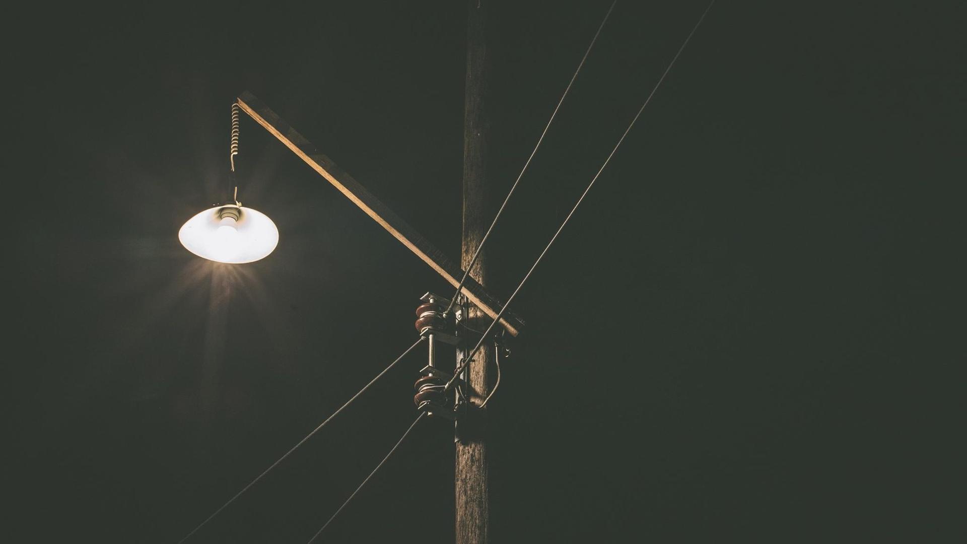Eine kleine Lampe leuchtet in der Dunkelheit an einem Strommast. Eine kleine Lampe leuchtet in der Dunkelheit an einem Strommast.