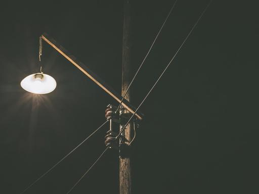 Eine kleine Lampe leuchtet in der Dunkelheit an einem Strommast.