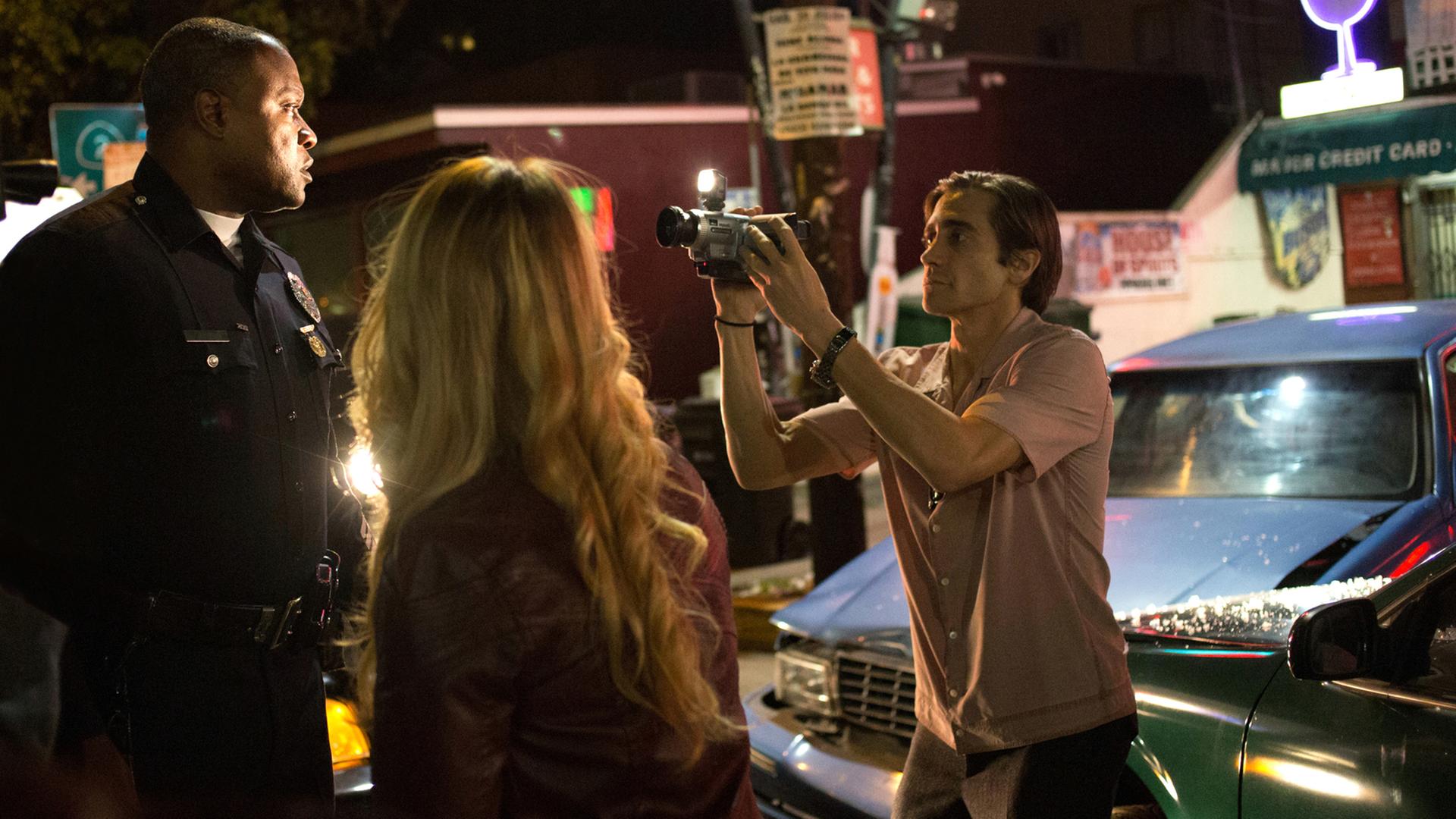 Die Szene des Films "Nightcrawler - Jede Nacht hat ihren Preis" zeigt den Kameramann Lou (Jake Gyllenhaal, r.) bei seiner rücksichtslosen Aufnahme eines Ereignisses auf der Straße. Die Szene des Films "Nightcrawler - Jede Nacht hat ihren Preis" zeigt den Kameramann Lou (Jake Gyllenhaal, r.) bei seiner rücksichtslosen Aufnahme eines Ereignisses auf der Straße.