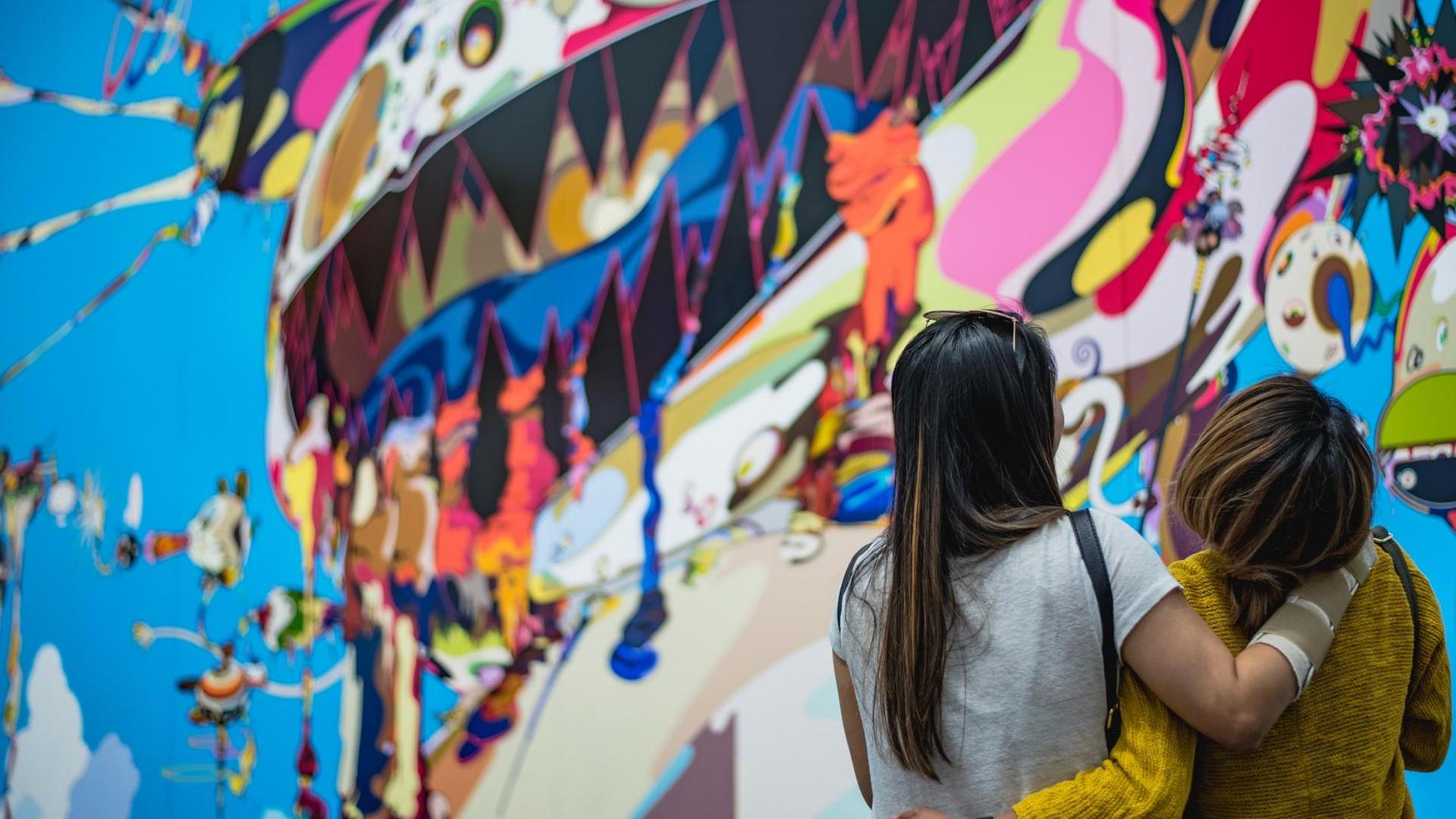 Zwei Frauen stehen lachend vor einem Street Art Kunstwerk und drehen uns den Rücken zu. Zwei Frauen stehen lachend vor einem Street Art Kunstwerk und drehen uns den Rücken zu.