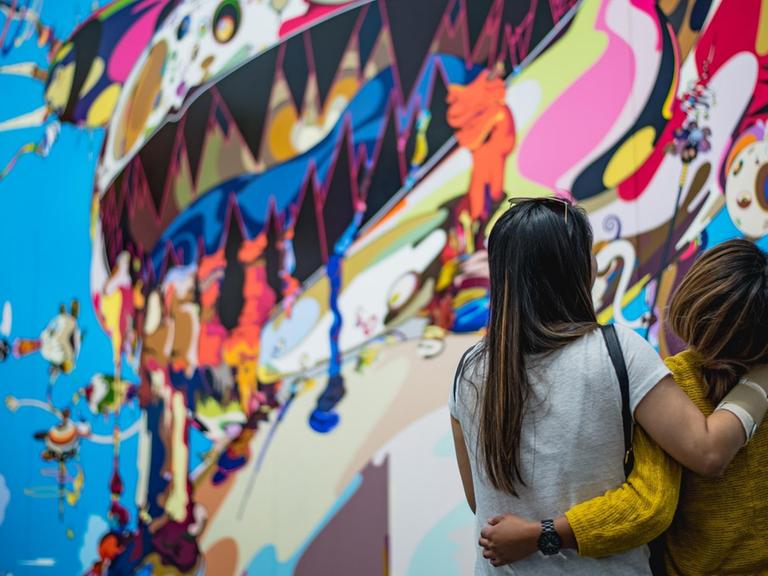 Zwei Frauen stehen lachend vor einem Street Art Kunstwerk und drehen uns den Rücken zu.