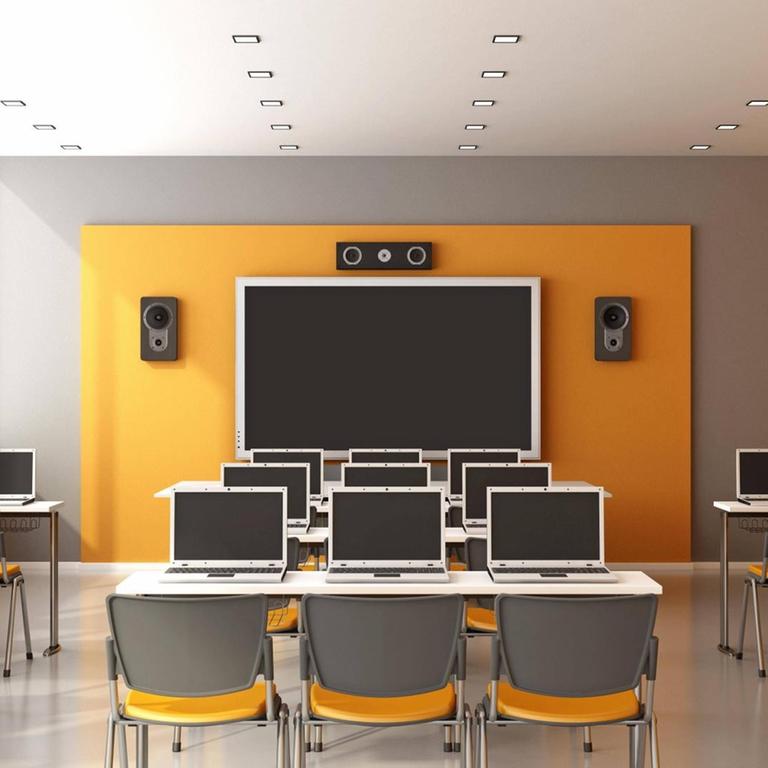 In einem Unterrichtsraum mit einer digitalen Tafel stehen Tischreihen mit Laptops