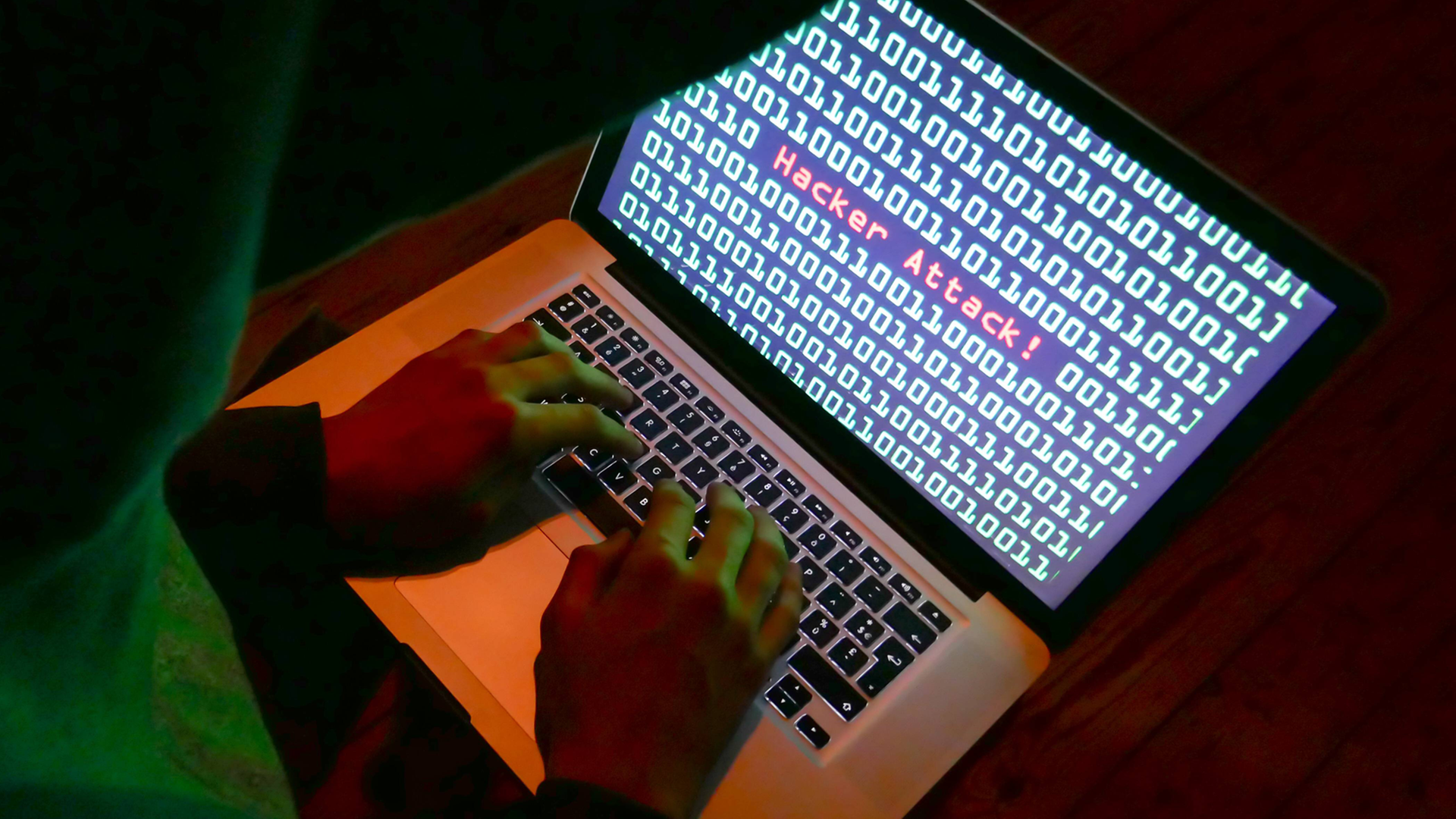 Symbolbild: Mensch sitzt vor einem Rechner, auf dem Bildschirm zu sehen: "Hacker Attack!"