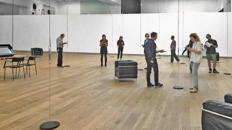 Installationsansicht "Radiophonic Spaces" im Museum Tinguely, Basel. Menschen stehen in einem Ausstellungsraum und haben Kopfhörer auf