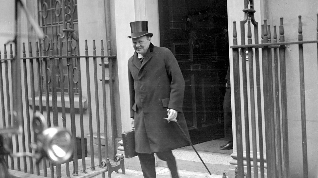 Winston Churchill verlässt das Gebäude mit Hut und Gehstock. Er grinst verschmitzt in die Kamera. Winston Churchill verlässt das Gebäude mit Hut und Gehstock. Er grinst verschmitzt in die Kamera.