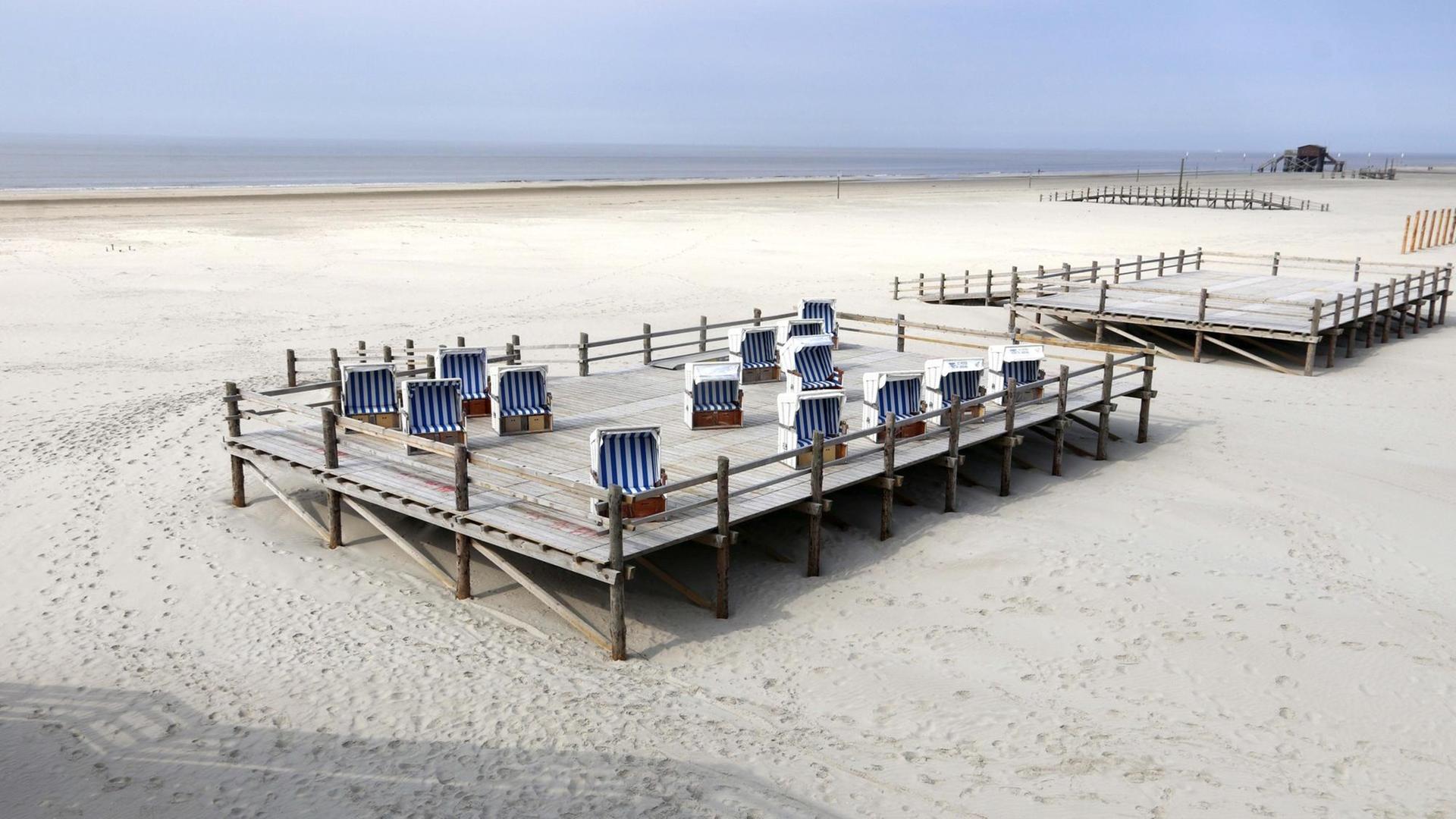 Am menschenleeren Strand von St. Peter-Ording stehen Strandkörbe auf einem Podest. Am menschenleeren Strand von St. Peter-Ording stehen Strandkörbe auf einem Podest.