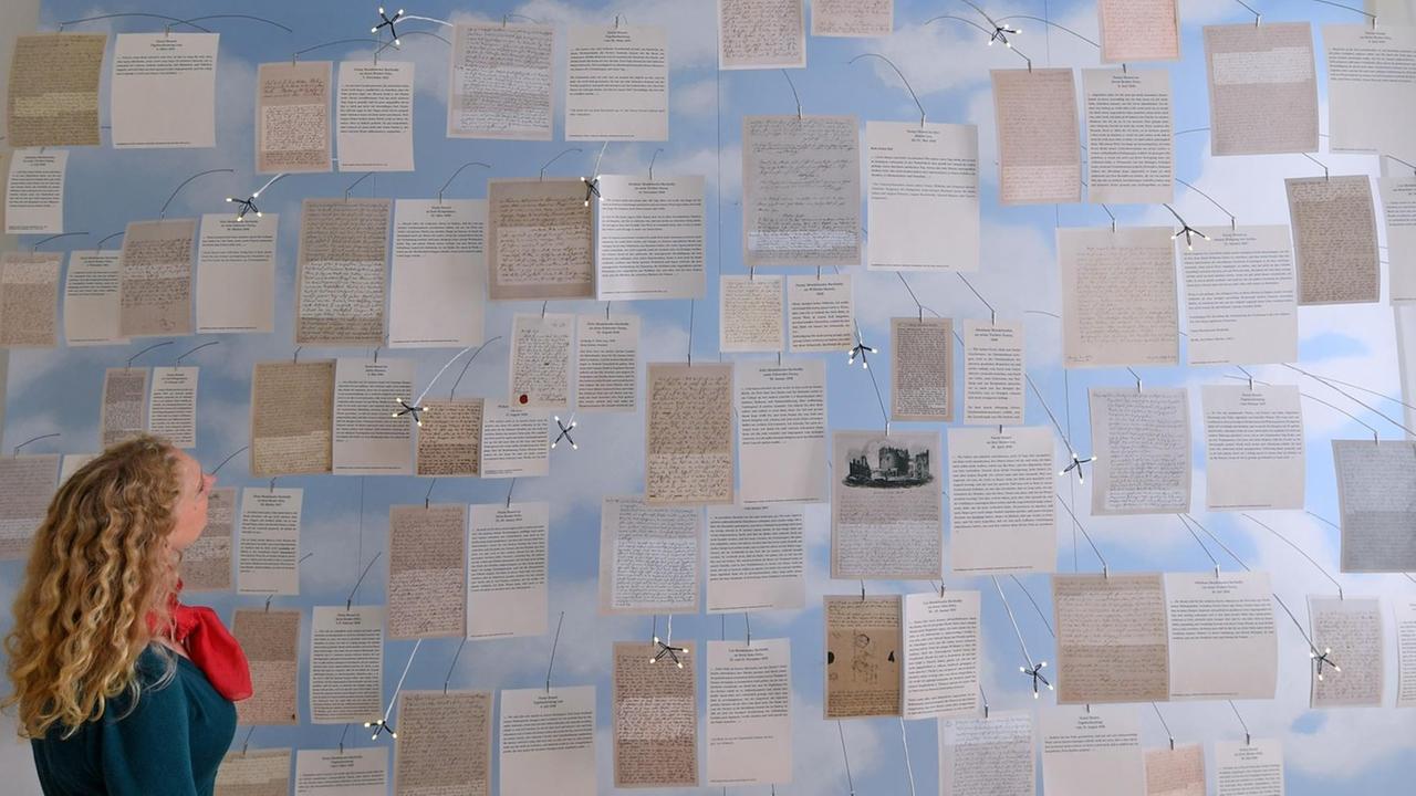 Eine Frau betrachtet in der Dauerausstellung des Mendelssohn-Haus in Leipzig die Schriftstücke aus dem Nachlass von Fanny Hensel, die von vielen Klammern gehalten werden. Eine Frau betrachtet in der Dauerausstellung des Mendelssohn-Haus in Leipzig die Schriftstücke aus dem Nachlass von Fanny Hensel, die von vielen Klammern gehalten werden.