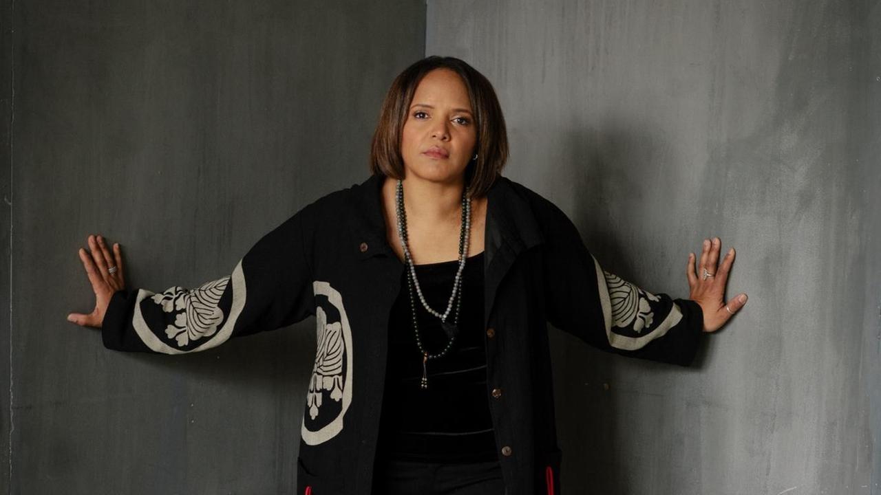 Porträt der US-Schlagzeugerin Terri Lyne Carrington. Sie steht in der Ecke zweier grauer Sichtbetonwände und berührte diese mit Ihren ausgestreckten Armen. Porträt der US-Schlagzeugerin Terri Lyne Carrington. Sie steht in der Ecke zweier grauer Sichtbetonwände und berührte diese mit Ihren ausgestreckten Armen.