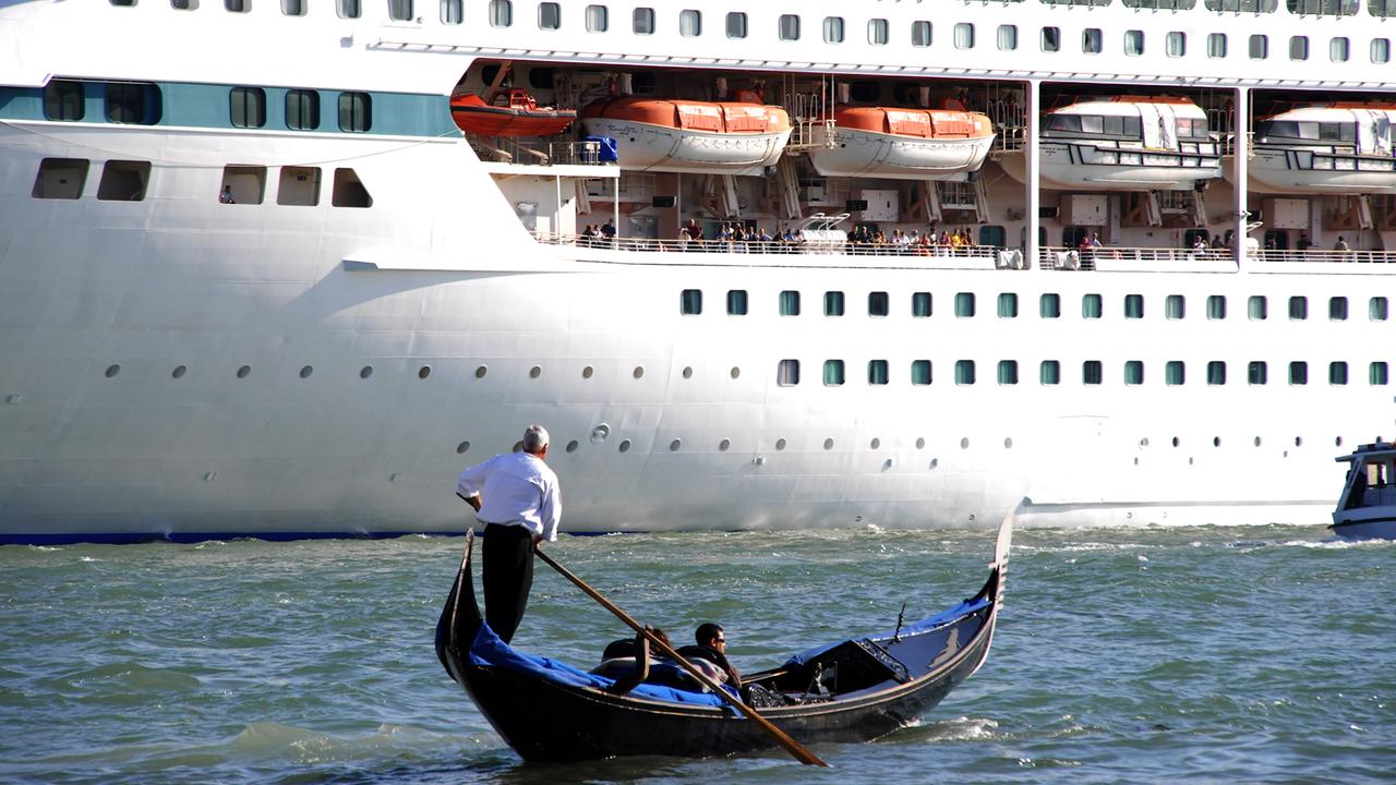 Ein Gondoliere mit zwei Touristen in seiner venezianischen Gondel vor dem riesigen Rumpf des 1.800 Passagiere fassenden Kreuzfahrtschiffes "Splendour of the Seas" auf dem Canale di San Marco, Venedig.