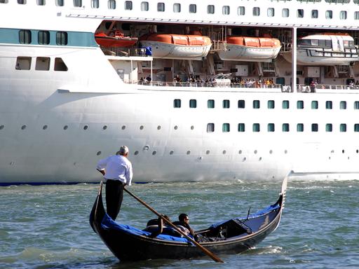 Ein Gondoliere mit zwei Touristen in seiner venezianischen Gondel vor dem riesigen Rumpf des 1.800 Passagiere fassenden Kreuzfahrtschiffes "Splendour of the Seas" (Royal Caribbean Cruise Line) auf dem Canale di San Marco, Venedig.