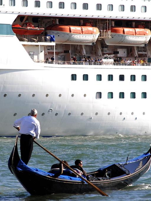 Ein Gondoliere mit zwei Touristen in seiner venezianischen Gondel vor dem riesigen Rumpf des 1.800 Passagiere fassenden Kreuzfahrtschiffes "Splendour of the Seas" (Royal Caribbean Cruise Line) auf dem Canale di San Marco, Venedig.