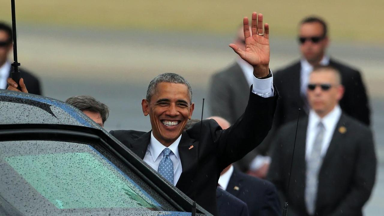 US-Präsident Barack Obama steht hinter einer schwarzen Limousine, strahlt und winkt. US-Präsident Barack Obama steht hinter einer schwarzen Limousine, strahlt und winkt.