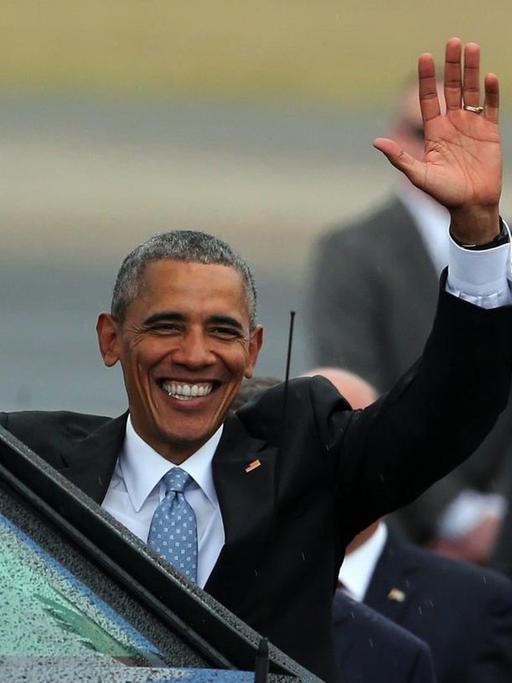 US-Präsident Barack Obama steht hinter einer schwarzen Limousine, strahlt und winkt.