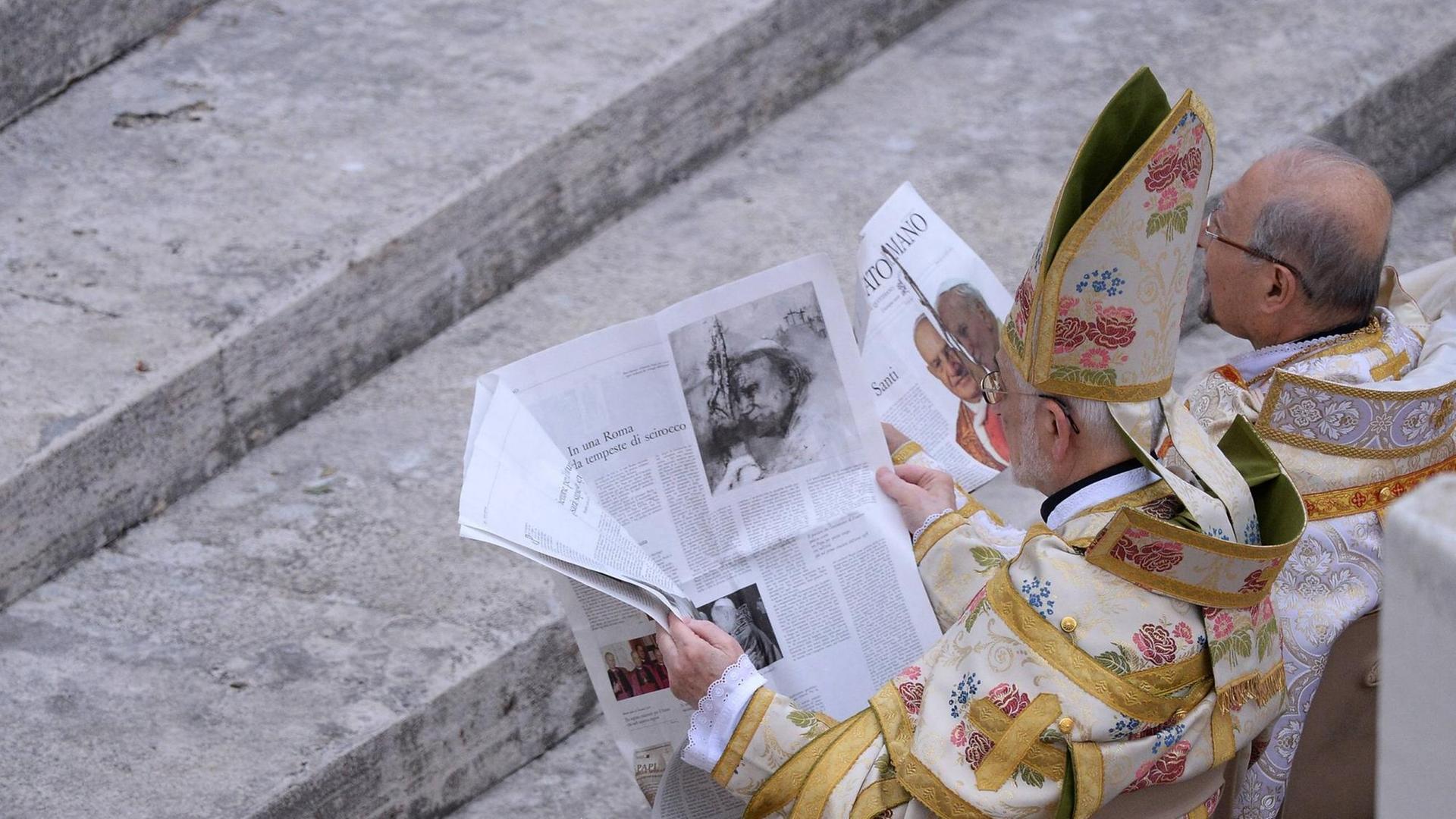 Zwei Bischoefe lesen am 27.04.2014 vor der Messe die aktuelle Ausgabe des "Osservatore Romano" auf dem Petersplatz.