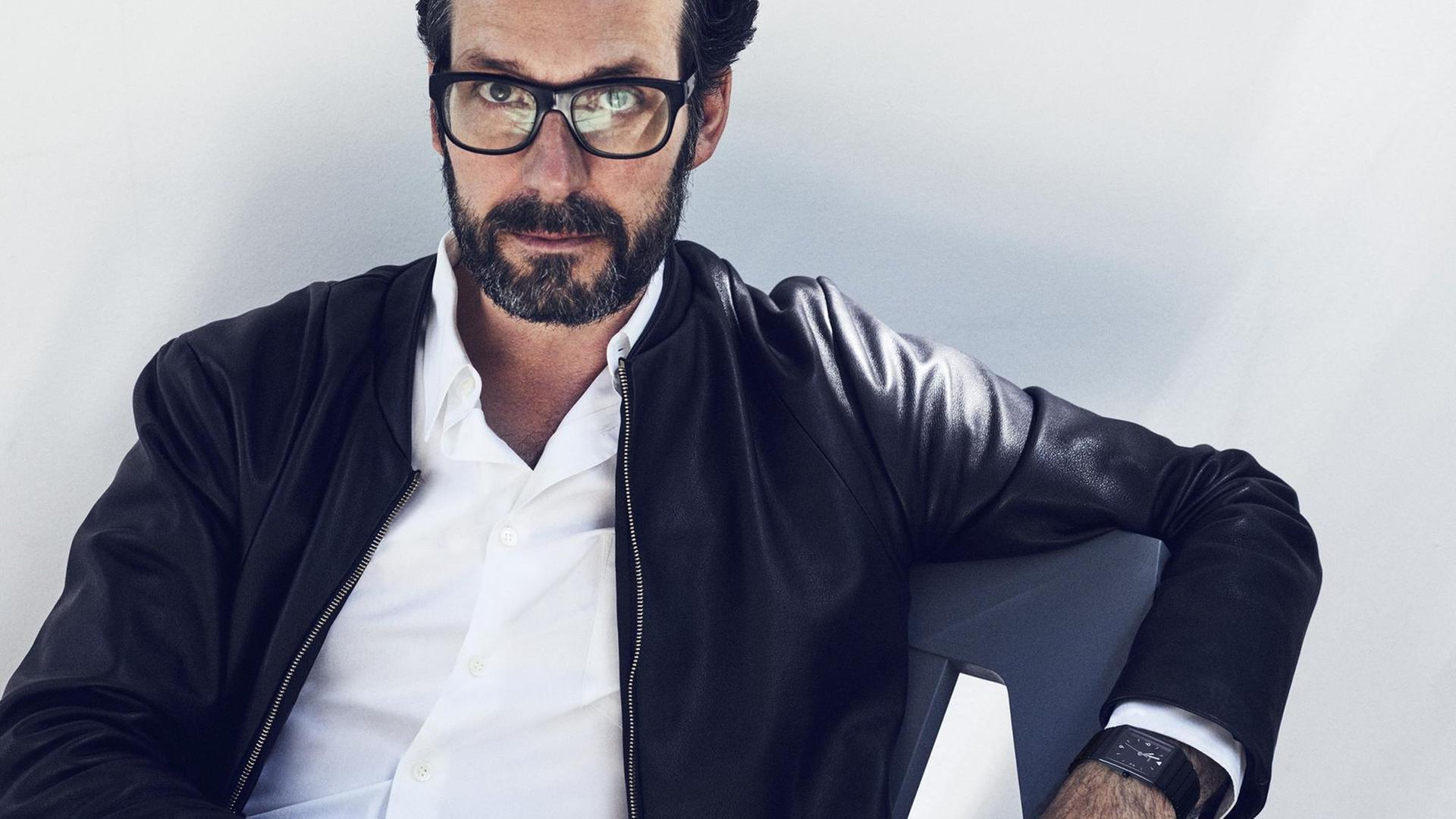 Porträt des Industrie-Designers Konstantin Cricic. Er trägt eine schwarze Lederjacke und sitzt in einem von ihm entworfenen Stuhl vor weißem Hintergrund. Porträt des Industrie-Designers Konstantin Cricic. Er trägt eine schwarze Lederjacke und sitzt in einem von ihm entworfenen Stuhl vor weißem Hintergrund.