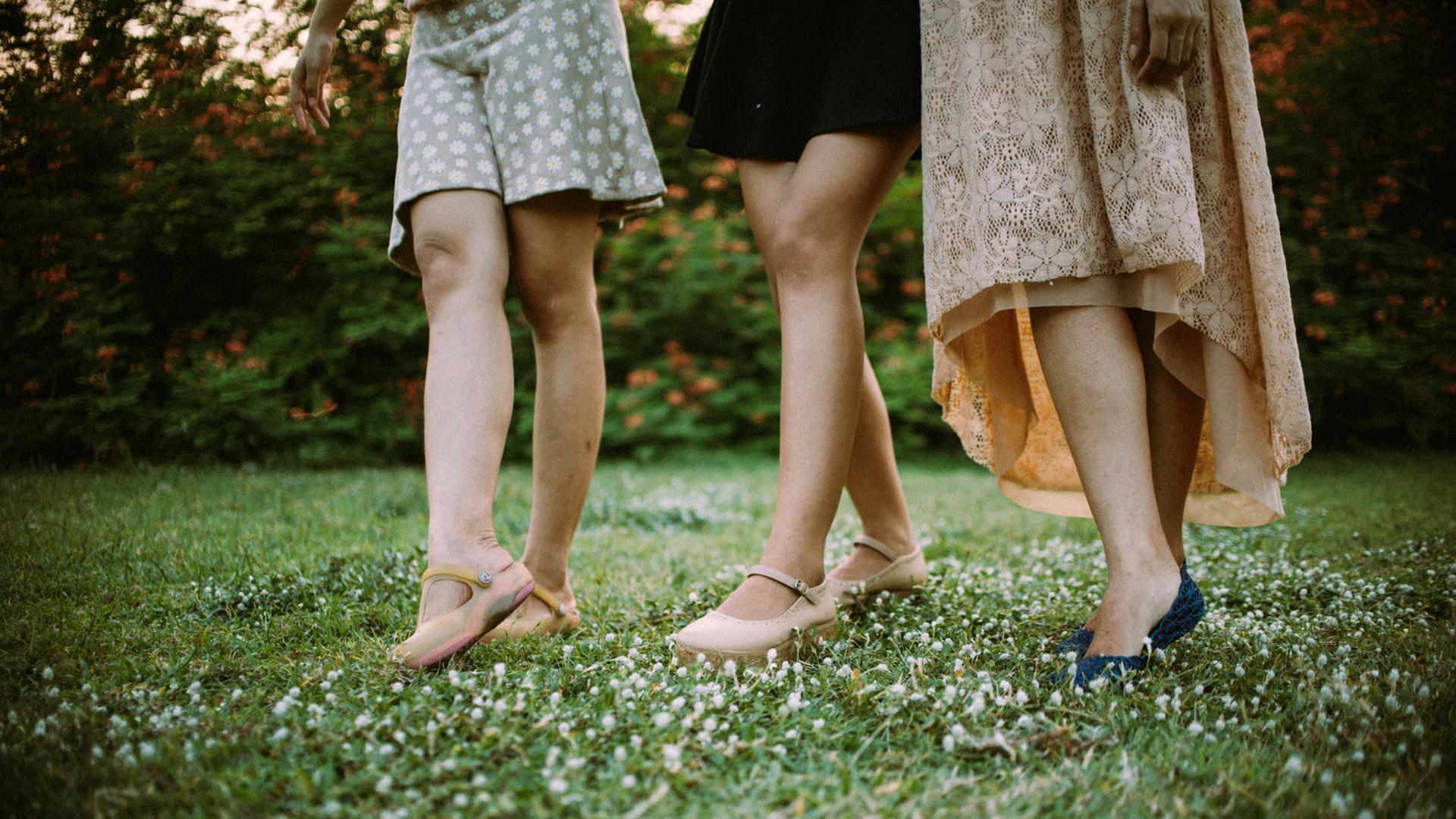 Die nackten Beine von drei Frauen in Röcken und Schuhen sind zu sehen. Sie spazieren über eine Wiese. Die nackten Beine von drei Frauen in Röcken und Schuhen sind zu sehen. Sie spazieren über eine Wiese.