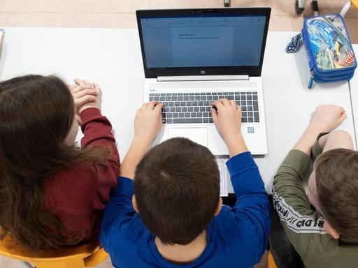 Schüler einer 3. Klasse sitzen in einem Klassenzimmer vor einem Laptop.