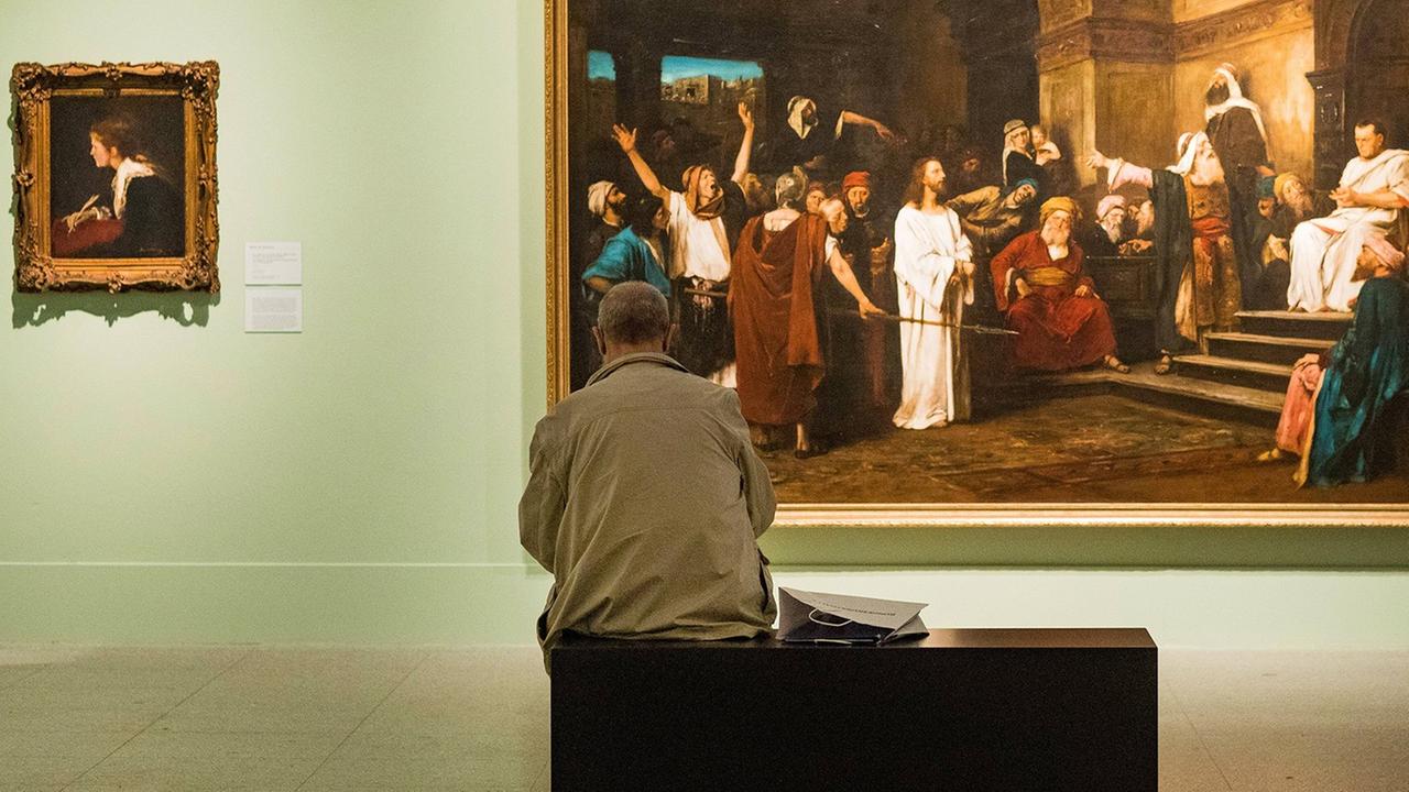 Ein Besucher sitzt in der Bundeskunsthalle mit dem Rücken zur Kamera vor einem Bild der Ausstellung "Malerfürsten"auf einer Bank.