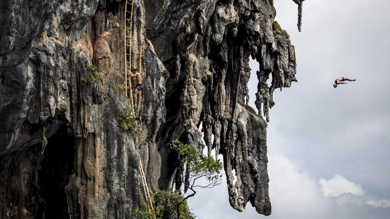 Ein Mann klettert an einer Bambusleiter an Klippen hoch, während ein anderer bereits im freien Fall ist. Ein Mann klettert an einer Bambusleiter an Klippen hoch, während ein anderer bereits im freien Fall ist.
