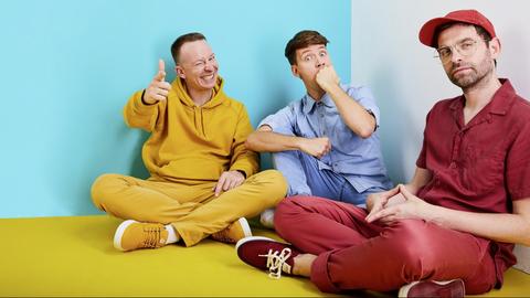 Ein Porträt der drei Bandmitglieder von "Deine Freunde" in farbenfroher Kleidung.