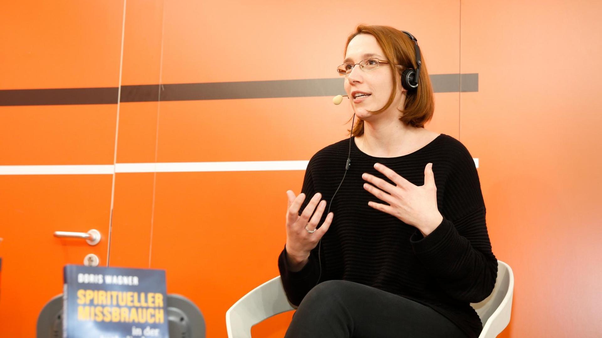 Doris Wagner auf der Bühne von Deutschlandfunk Kultur mit Mikrofon, gestikulierend. Doris Wagner auf der Bühne von Deutschlandfunk Kultur mit Mikrofon, gestikulierend.