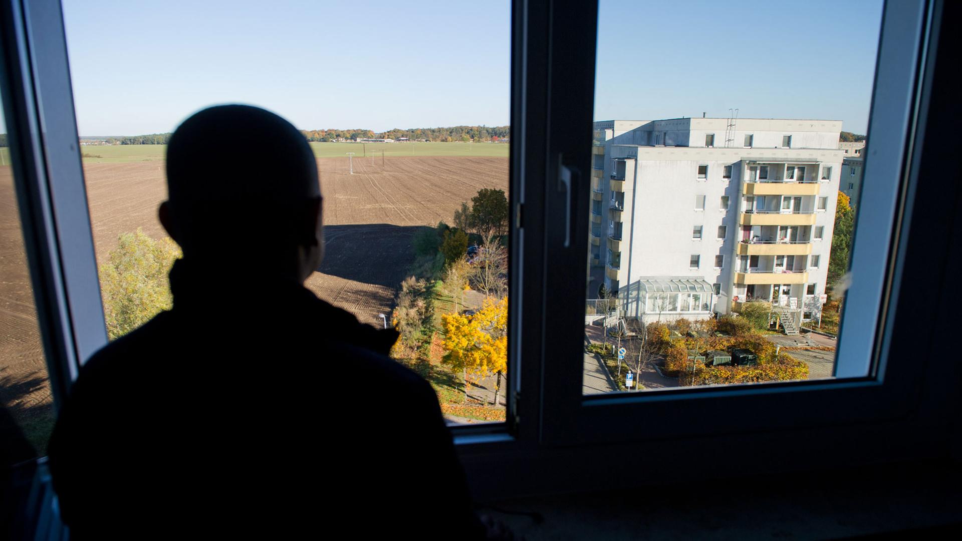 Ein Asylbewerber blickt am 26.10.2012 aus einem Fenster eines Asylbewerberheims in Wolgast in Mecklenburg-Vorpommern. Vor dem Fenster ist ein Plattenbau und flache Landschaft mit Äckern, Wiesen und Wald zu sehen. Ein Asylbewerber blickt am 26.10.2012 aus einem Fenster eines Asylbewerberheims in Wolgast in Mecklenburg-Vorpommern. Vor dem Fenster ist ein Plattenbau und flache Landschaft mit Äckern, Wiesen und Wald zu sehen.