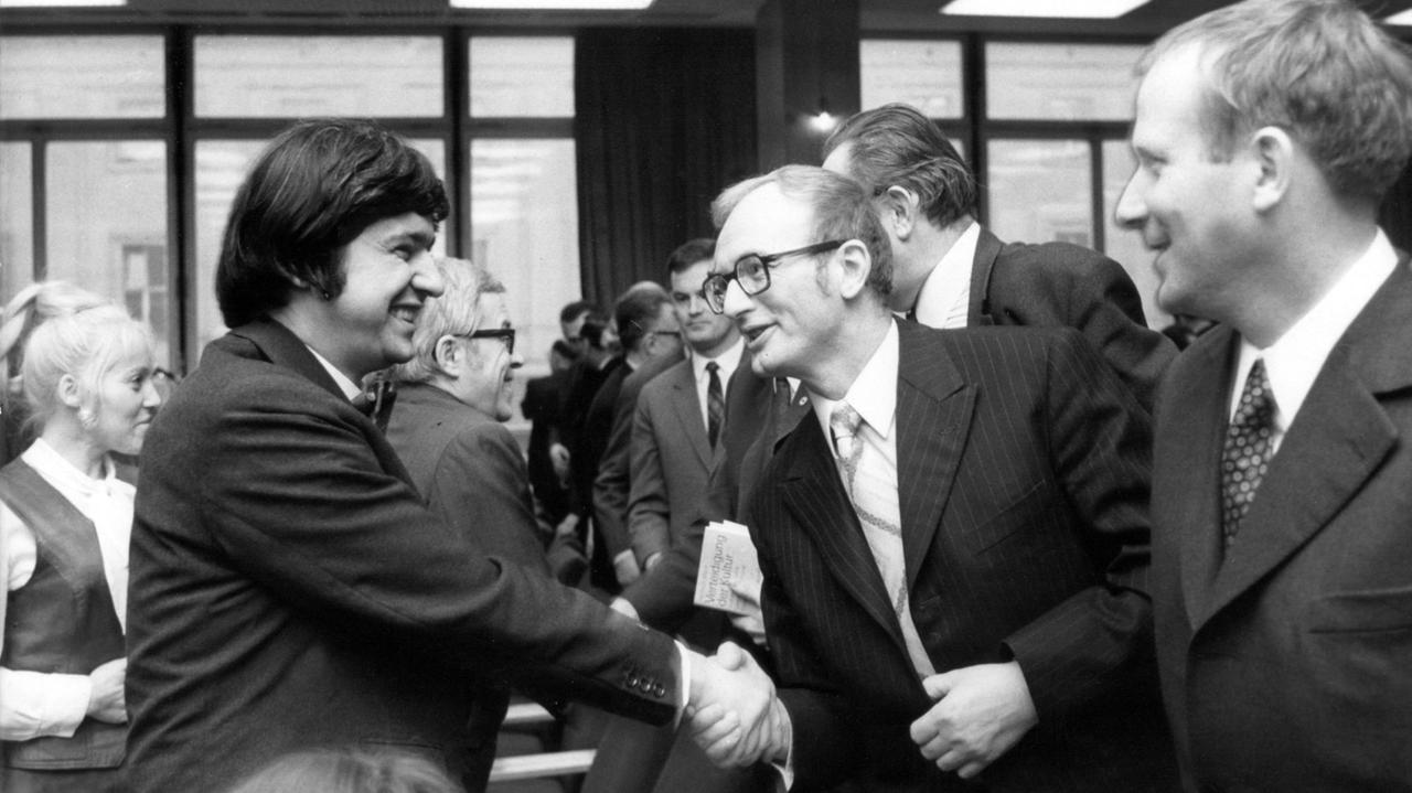 Der Schriftsteller Hermann Kant (l) beglückwünscht seinen Kollegen Jurek Becker (M) im März 1971 zum Heinrich-Mann-Preis während der Eröffnung einer Heinrich-Mann-Ausstellung in der Ost-Berliner Stadtbibliothek.