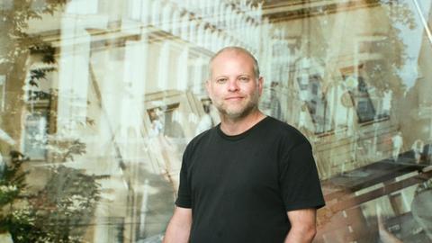 Autor Kristof Magnusson im schwarzen T-Shirt. Im Hintergrund spiegeln sich Gebäude.