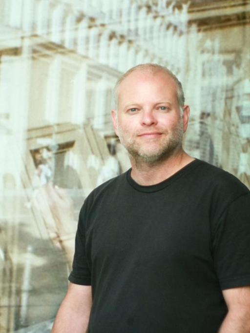 Autor Kristof Magnusson im schwarzen T-Shirt. Im Hintergrund spiegeln sich Gebäude.