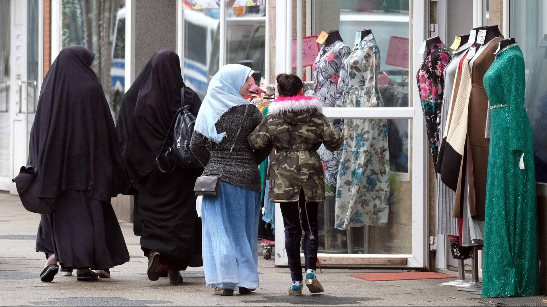 Zwei in schwarz verhüllte ältere Frauen und zwei jüngere Mädchen, davon eins mit mit Kopftuch, passieren ein muslimisches Bekleidungsgeschäft mit Schaufensterpuppen in Duisburg-Marxloh. Zwei in schwarz verhüllte ältere Frauen und zwei jüngere Mädchen, davon eins mit mit Kopftuch, passieren ein muslimisches Bekleidungsgeschäft mit Schaufensterpuppen in Duisburg-Marxloh.