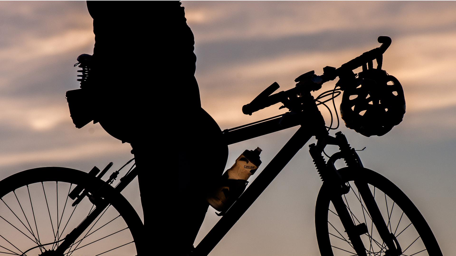 Radfahrerin im Abendlicht. Ihr Helm hängt an der Lenkstange.