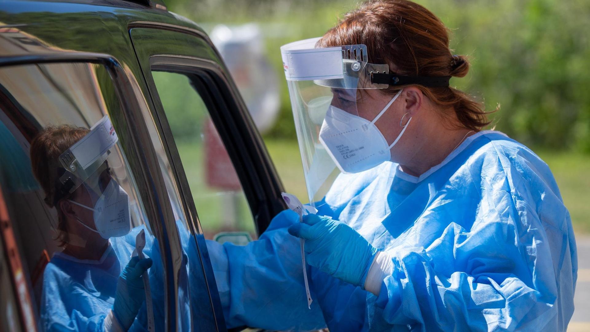 Eine Mitarbeiterin des Testzentums Covid Control Rügen steht neben einem PKW und testet durchs Autofenster eine Person auf Covid-19. Eine Mitarbeiterin des Testzentums Covid Control Rügen steht neben einem PKW und testet durchs Autofenster eine Person auf Covid-19.