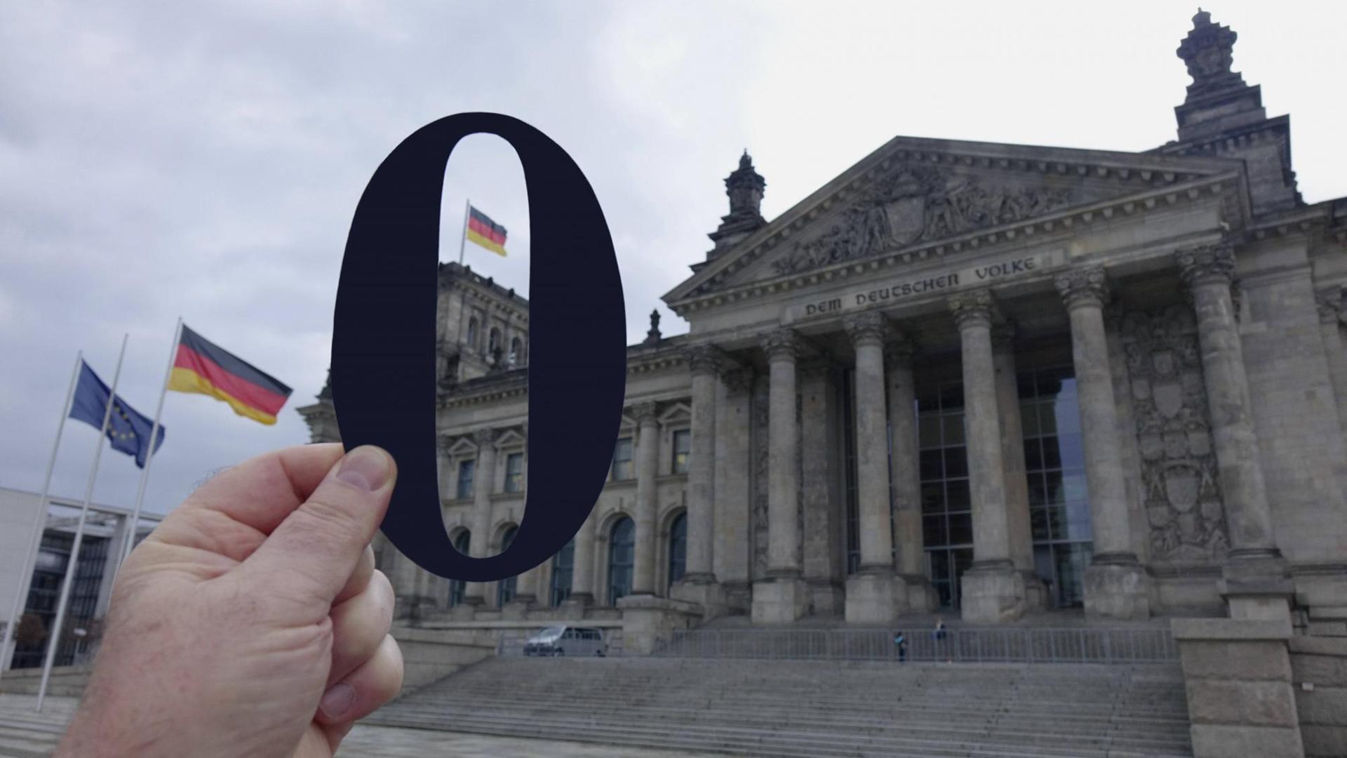 Eine Hand Hält eine ausgeschnittene schwarze Null vor den Reichstag.