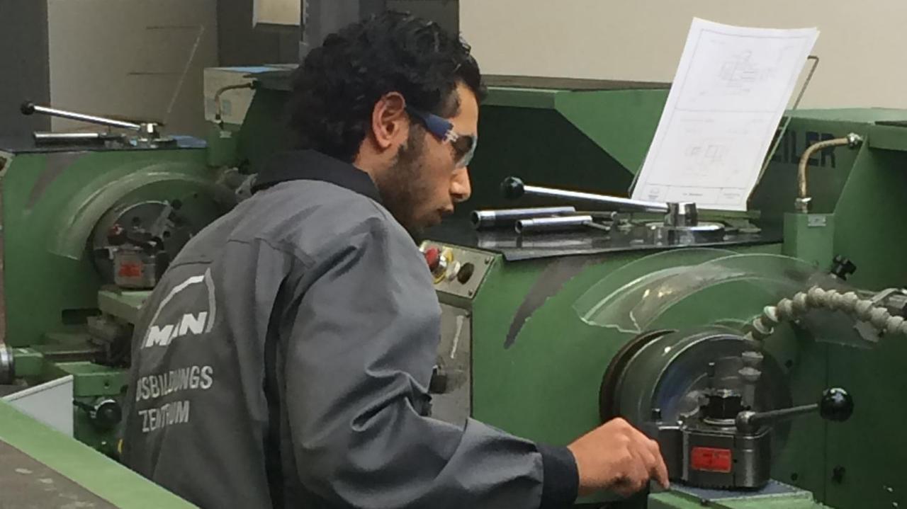 Der Auszubildende sitzt im grauen Overall und Schutzbrille einer grünen Maschine an einer Maschine. Der Auszubildende sitzt im grauen Overall und Schutzbrille einer grünen Maschine an einer Maschine.