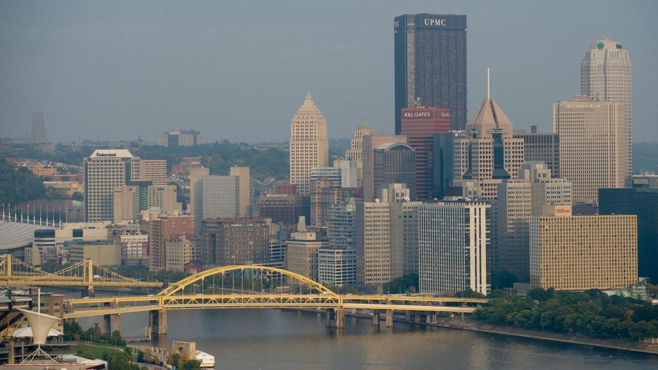 Stadtansicht von Pittsburgh im US-Bundesstaat Pennsylvania - im Vordergrund der Skyline sind ein Fluss und eine Brücke zu sehen.