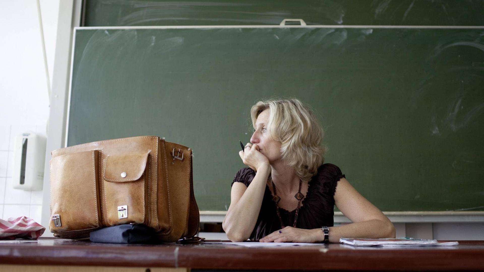 Eine Lehrerin sitzt vor einer leeren Tafel und schaut aus dem Fenster Eine Lehrerin sitzt vor einer leeren Tafel und schaut aus dem Fenster