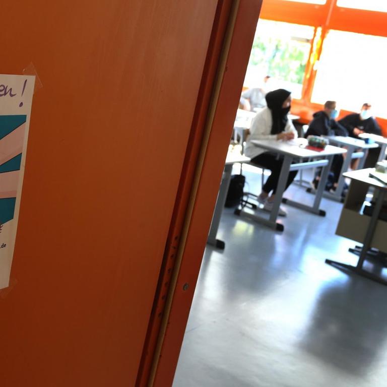 Schüler einer neunten Klasse einer Mittelschule sitzen am ersten Schultag zu Beginn des Unterrichts mit Mundschutz neben einem Schild das auf Abstand halten erinnert.