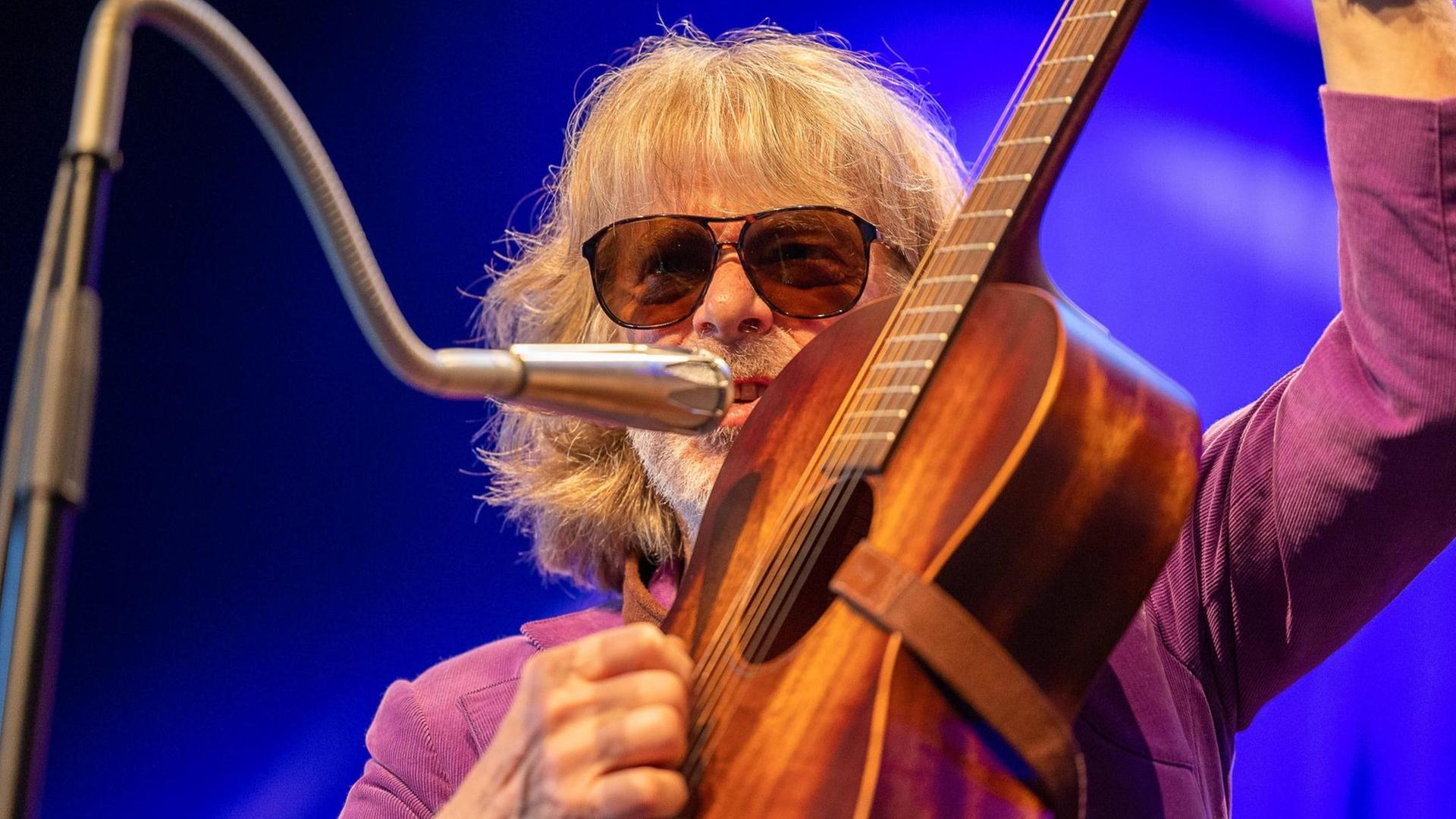 Helge Schneider singt in ein Schwanenhalsmikrofon und spielt auf einer Akustikgitarre. Helge Schneider singt in ein Schwanenhalsmikrofon und spielt auf einer Akustikgitarre.