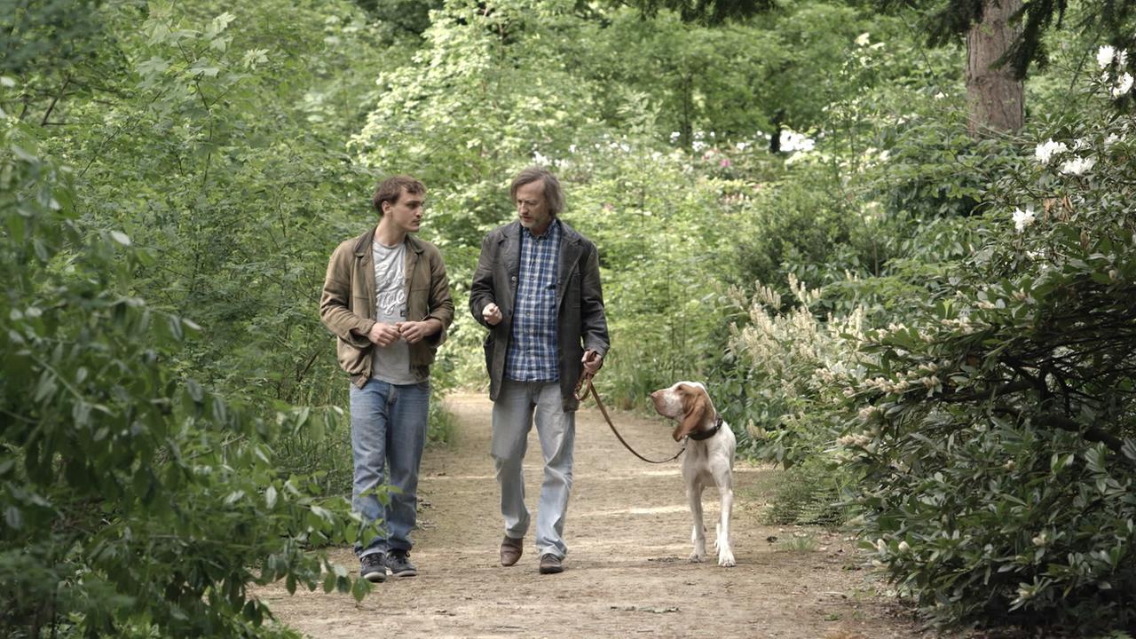 Szenenbild aus Fikkefuchs: Thorben (Franz Rogowski) und Rocky (Jan Henrik Stahlberg) gehen mit dem Hund im Park spazieren