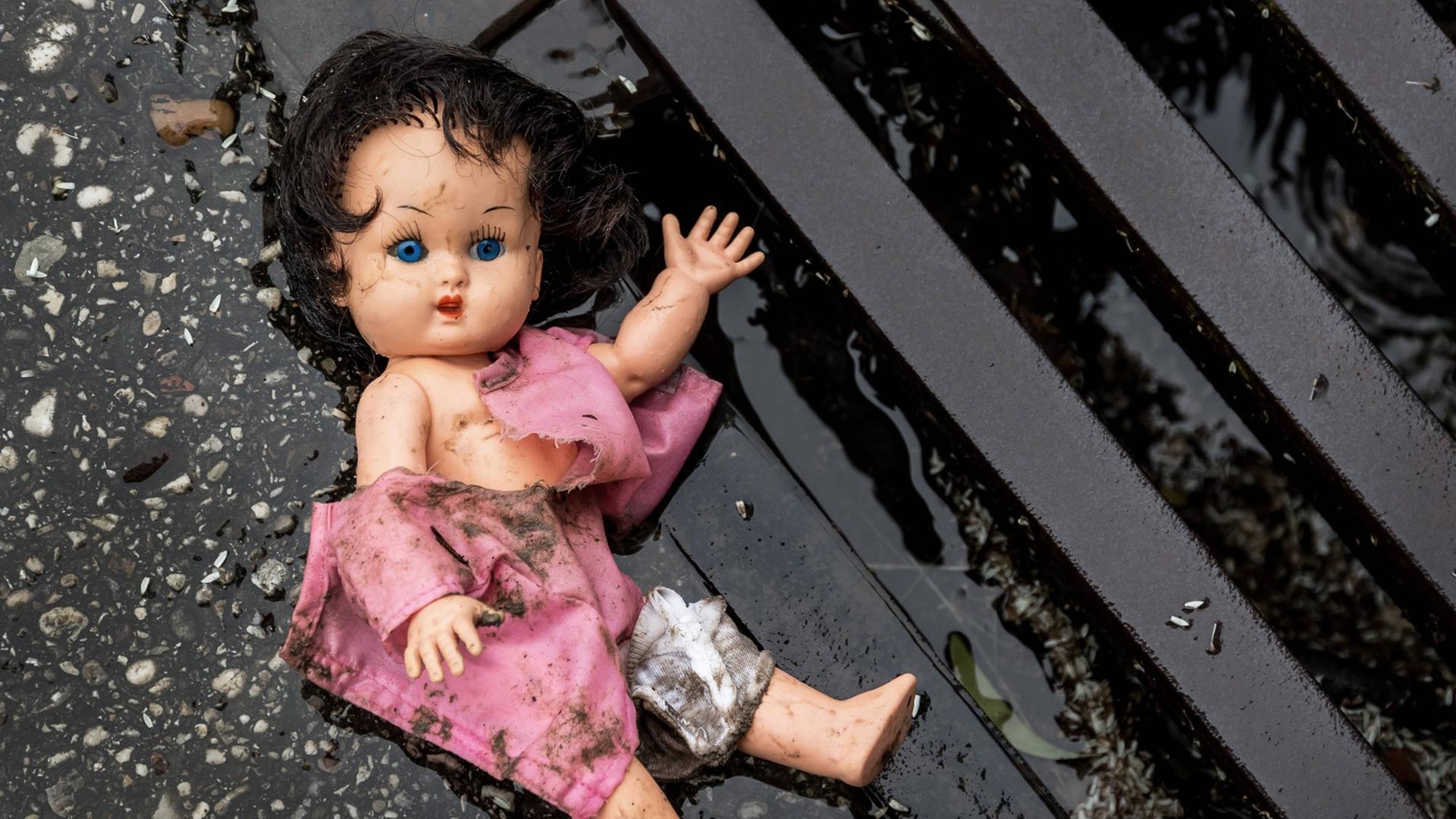 Eine Puppe liegt in dreckiger Bekleidung an einem Straßengully. Eine Puppe liegt in dreckiger Bekleidung an einem Straßengully.