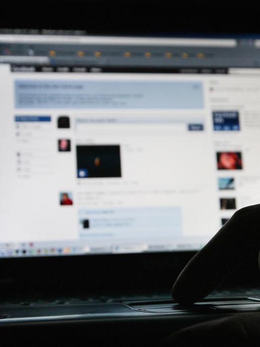 Ein heller und unscharfer Computerbilschirm, mit einer offenen Facebookseite und einer Handsilhouette an der Tastatur.