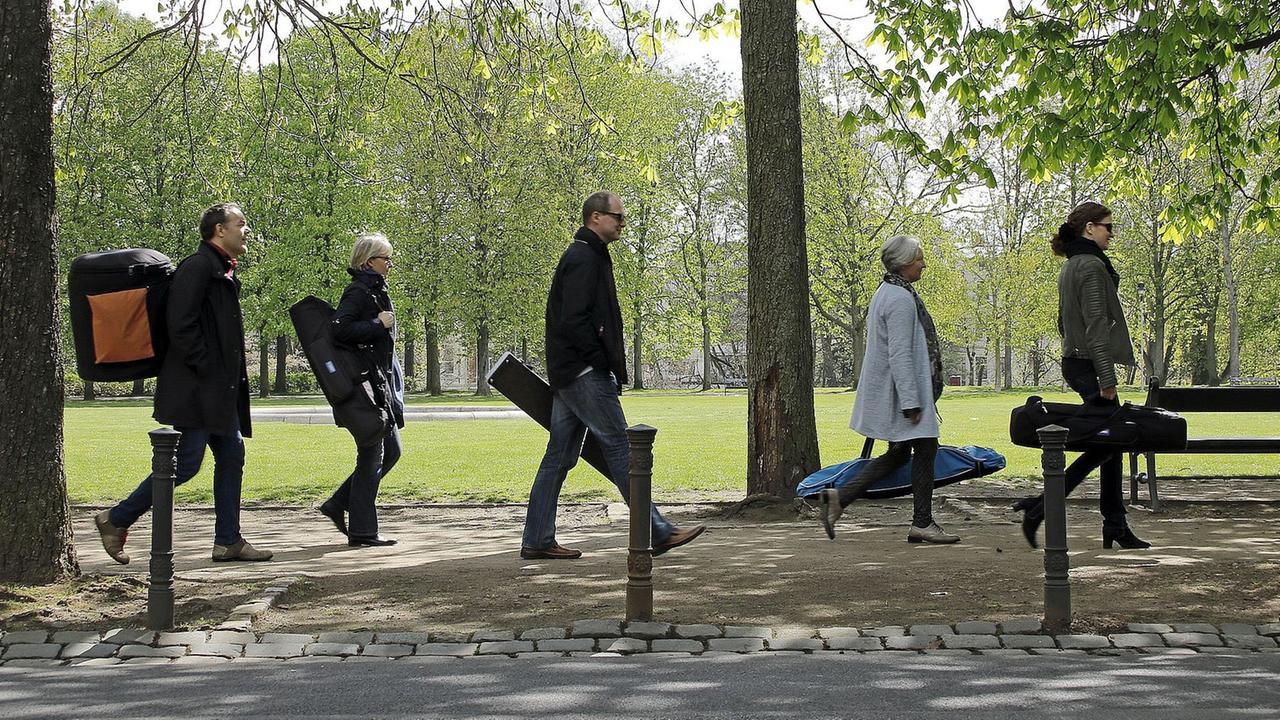 Fünf Musiker laufen mit Gepäck hintereinander durch einen Park. Fünf Musiker laufen mit Gepäck hintereinander durch einen Park.