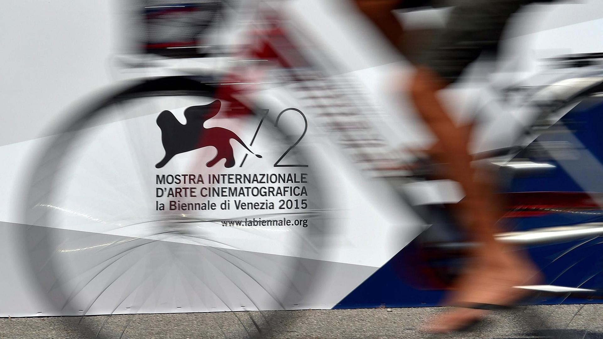 Vor dem offiziellen Logo der 72. Filmfetspiele in Venedig 2015 fährt ein Mann Fahrrad. Schemenhaft sind die Beine und das Fahrrad zu sehen. Vor dem offiziellen Logo der 72. Filmfetspiele in Venedig 2015 fährt ein Mann Fahrrad. Schemenhaft sind die Beine und das Fahrrad zu sehen.