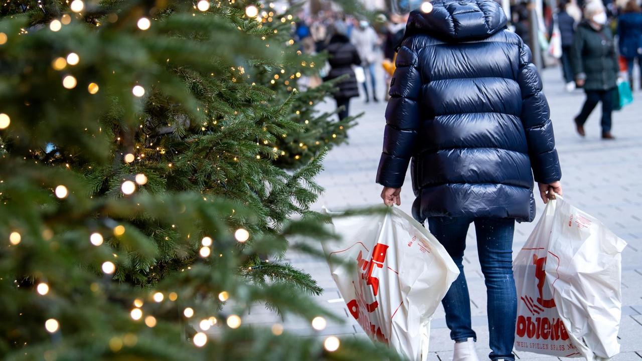 Ein Mann ist in der mit einer weihnachtlichen Tanne geschmückten Fußgängerzone mit seinen Einkäufen unterwegs. Ein Mann ist in der mit einer weihnachtlichen Tanne geschmückten Fußgängerzone mit seinen Einkäufen unterwegs.