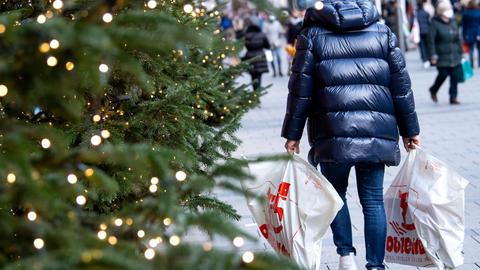 Ein Mann ist in der mit einer weihnachtlichen Tanne geschmückten Fußgängerzone mit seinen Einkäufen unterwegs.