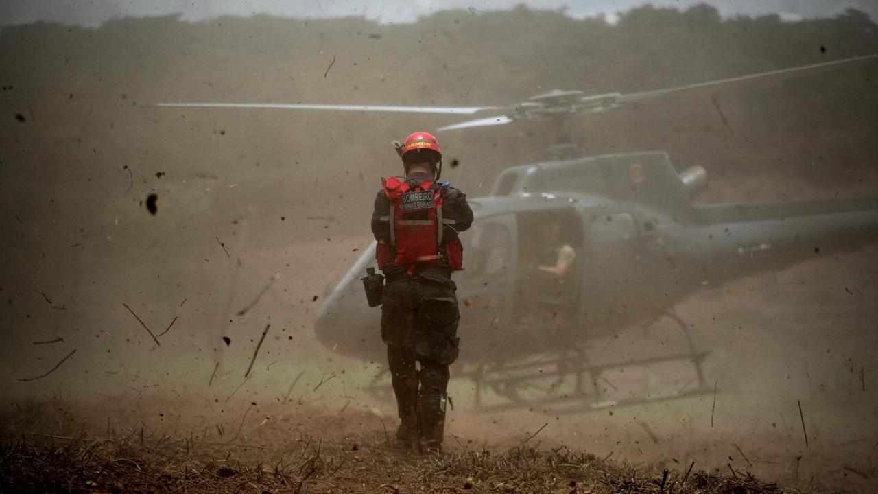 Ein Helfer steht während des Rettungseinsatzes vor einem Hubschrauber 