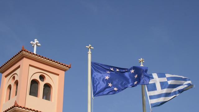 Europäische und griechische Flagge vor dem Kirchturm im Bergdorf Pano Hersonissos auf der griechischen Insel Kreta.