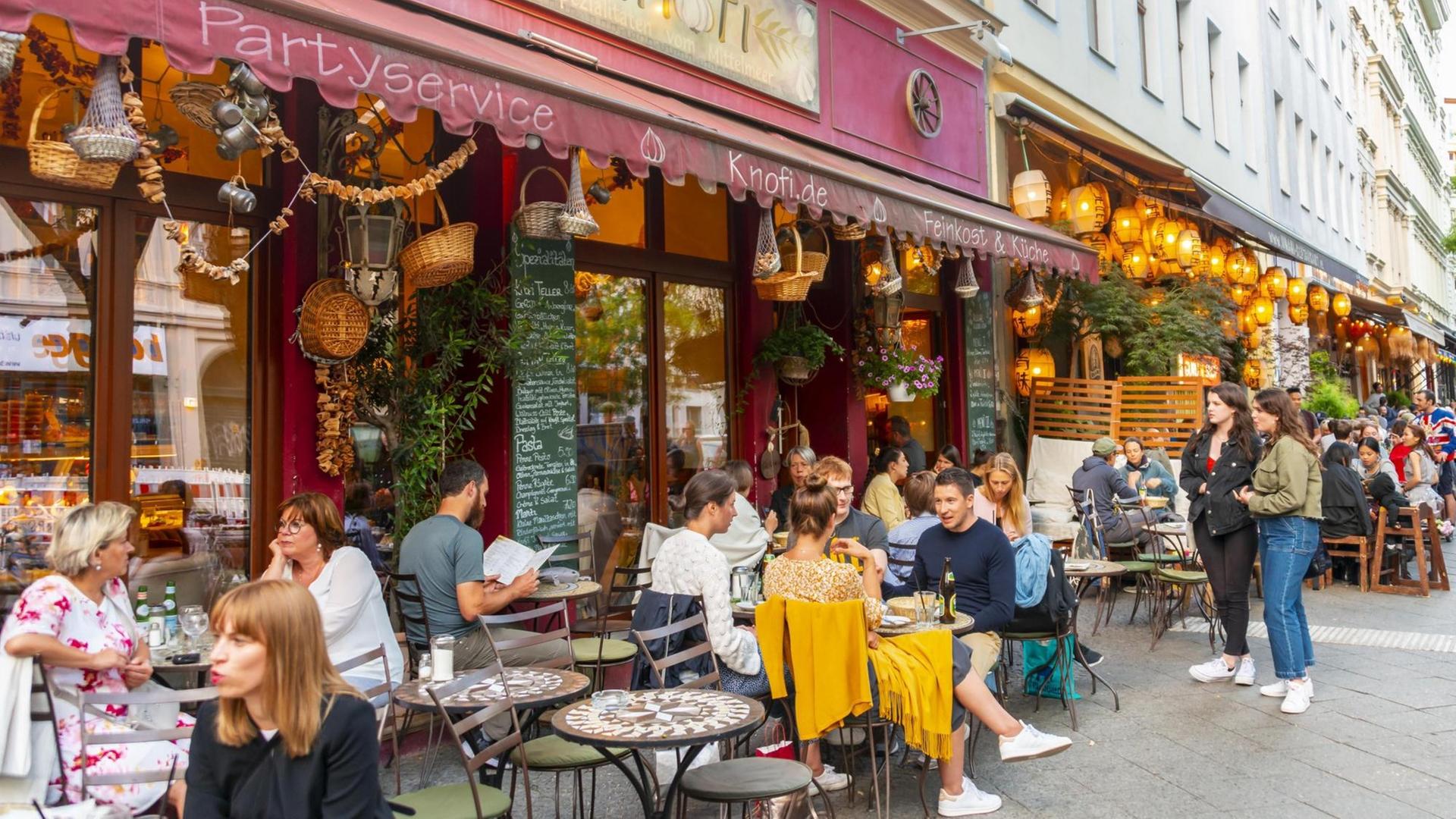 Menschen sitzen an Tischen draußen vor dem Restaurant Knofi in der bei Touristen beliebten Bergmannstraße in Berlin-Kreuzberg. Verwendung weltweit, Keine Weitergabe an Wiederverkäufer. Menschen sitzen an Tischen draußen vor dem Restaurant Knofi in der bei Touristen beliebten Bergmannstraße in Berlin-Kreuzberg. Verwendung weltweit, Keine Weitergabe an Wiederverkäufer.