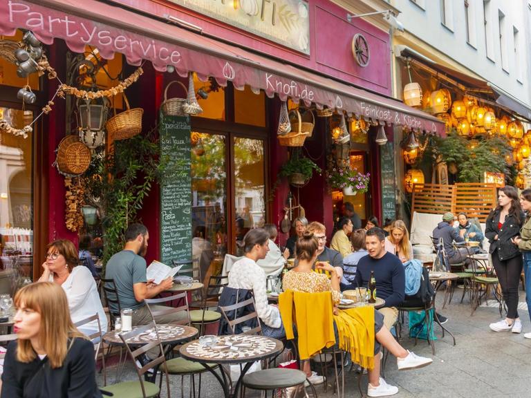 Menschen sitzen an Tischen draußen vor dem Restaurant Knofi in der bei Touristen beliebten Bergmannstraße in Berlin-Kreuzberg. Verwendung weltweit, Keine Weitergabe an Wiederverkäufer.